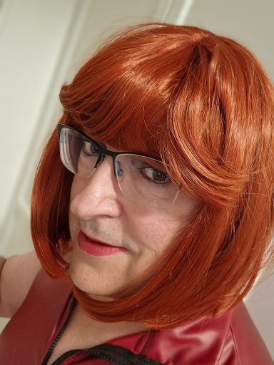 Ich, mit rotem Haarschnitt und Brille, trage Lippenstift und ein rotes Oberteil.